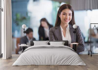 Portrait of successful young Asian businesswoman at office, colleagues in background. Wall mural